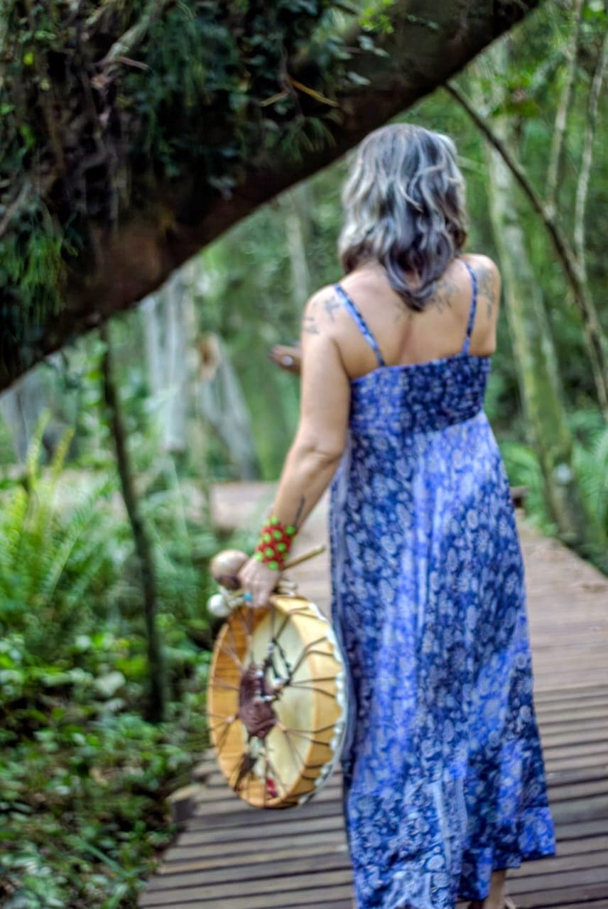 Mulher caminhando pela floresta com tambor xamânico
